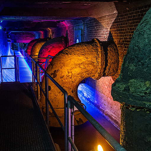 Unterirdischer Teil der Ausstellung mit großen Abwasserrohrren, bunt beleuchtet
